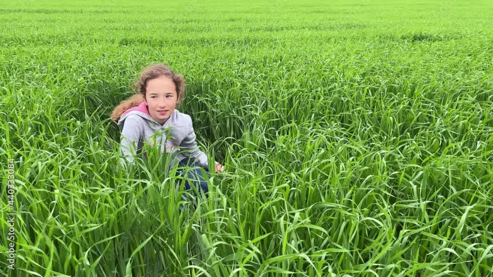 4k Cute small girl sitting on a green grass, smiling and looking around. 4k Cute small girl sitting on a green grass, smiling and looking around.