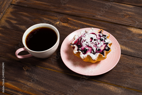 Fresh black coffee in a cup. Cake basket with cottage cheese and berries, sprinkled with powdered sugar. Breakfast on the background of a table made of dark wood.
