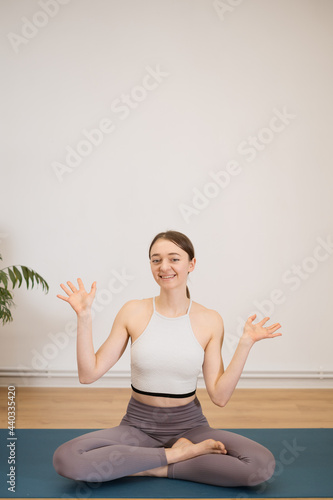 Fototapeta Naklejka Na Ścianę i Meble -  Sporty young woman doing yoga practice on white wall background with plants - concept of healthy life and natural balance between body and mental development
