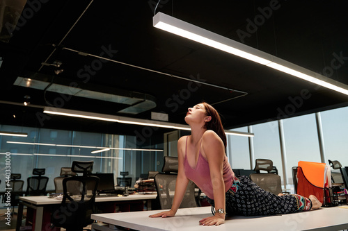 portrait of young woman doing yoga on the table, inside the work office, zen state and relaxation inside the work place. stress control. healthy life concept.