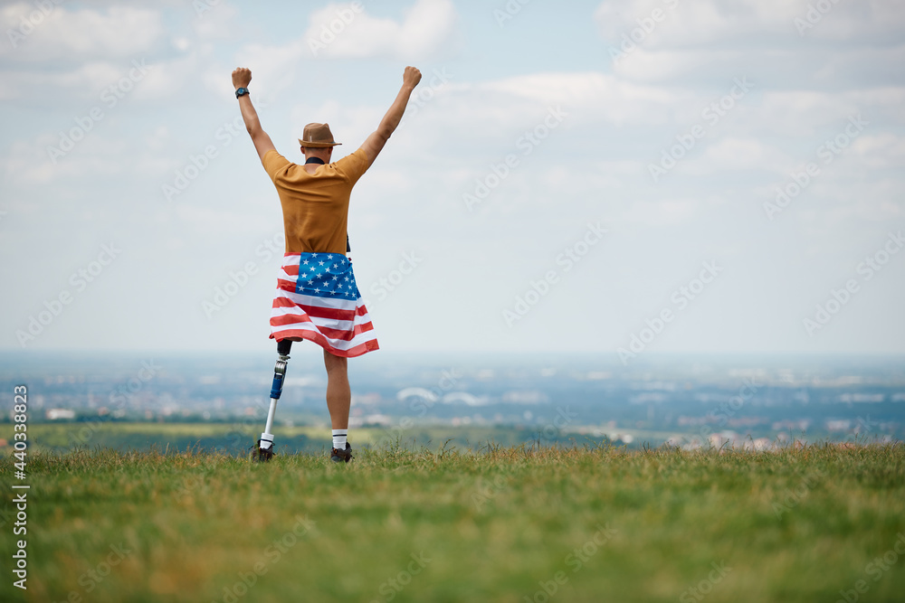 Rear view of disabled American man with leg prosthesis stands with raised arms on top of hill. Copy space. Rear view of disabled American man with leg prosthesis stands with raised arms on top of hill. Copy space.