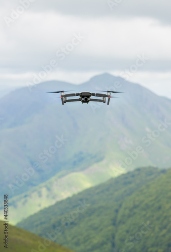 Drone flying over mountainous landscape. The drone can be seen from the front and the camera has an ND filter. In the background you can see a mountain and at the bottom a forest and a green meadow.