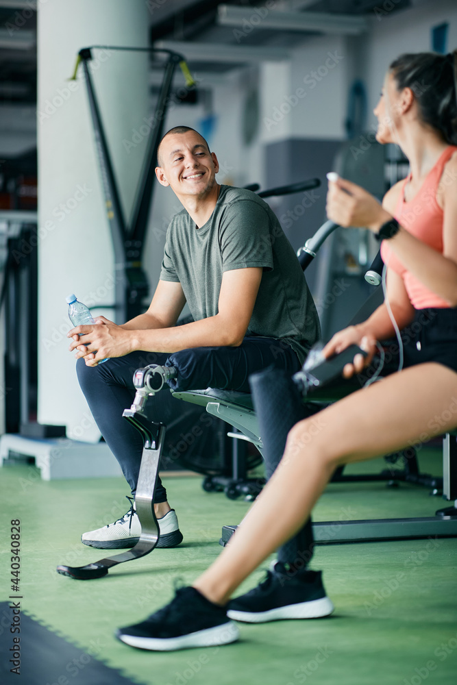 Happy sportsman with prosthetic leg and his female friend talking while taking a break from exercising at gym. Happy sportsman with prosthetic leg and his female friend talking while taking a break from exercising at gym.