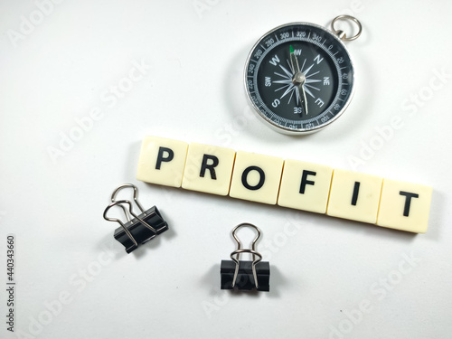 Selective focus.Scrabble letters with text PROFIT with compass and paper clips on white background.