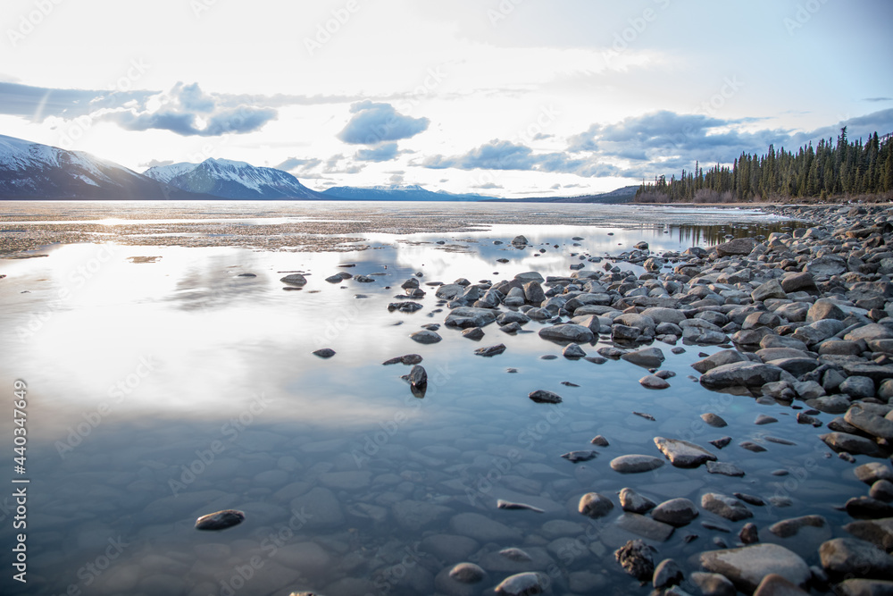 Stunning Canadian lake view in spring summer taken in British Columbia, Atlin with cloudy, blue sky and perfect calm reflection water snow capped mountains scenery. 