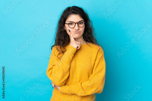 Teenager Russian girl isolated on blue background and thinking