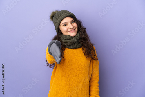 Teenager Russian girl with winter hat isolated on purple background shaking hands for closing a good deal