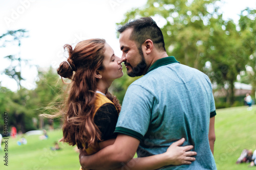 young hispanic latin couple of a white girl with red hair and a boy with a beard and short hair are hugging in a park. © SETO fotografias
