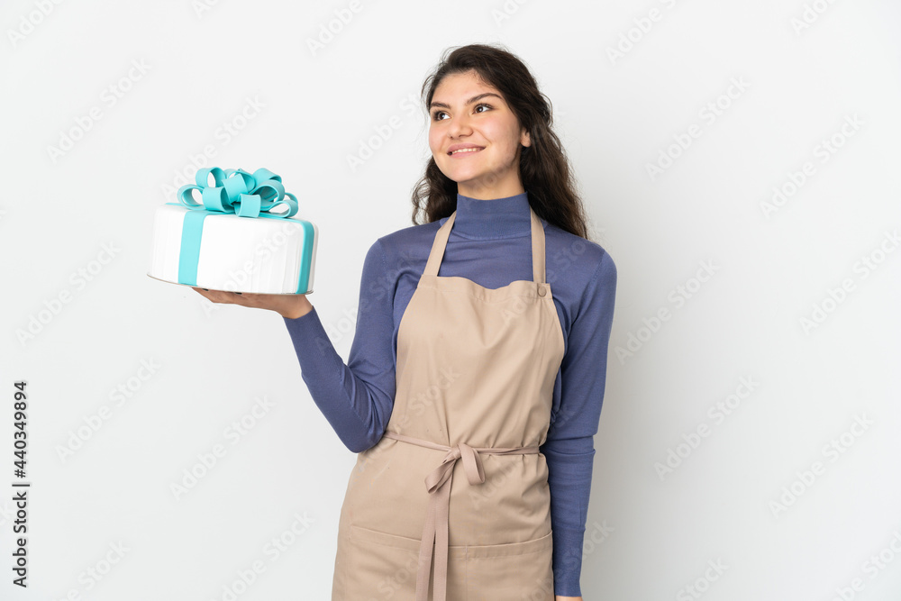 Pastry Russian chef holding a big cake isolated on white background thinking an idea while looking up Pastry Russian chef holding a big cake isolated on white background thinking an idea while looking up