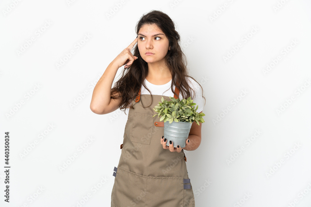 Young Russian gardener girl holding a plant isolated having doubts and thinking