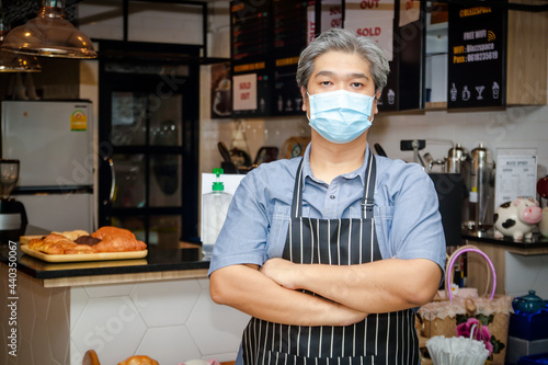 Asian elderly men wearing blue masks running a coffee shop business Wear an apron standing at the bar counter. Entrepreneurship concept, doing business during the coronavirus pandemic