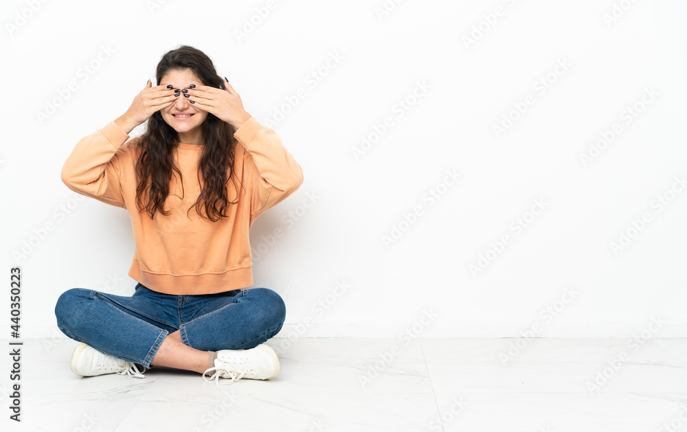 Teenager Russian girl sitting on the floor covering eyes by hands and smiling Teenager Russian girl sitting on the floor covering eyes by hands and smiling