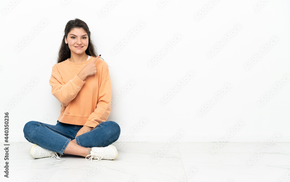 Teenager Russian girl sitting on the floor pointing to the side to present a product Teenager Russian girl sitting on the floor pointing to the side to present a product