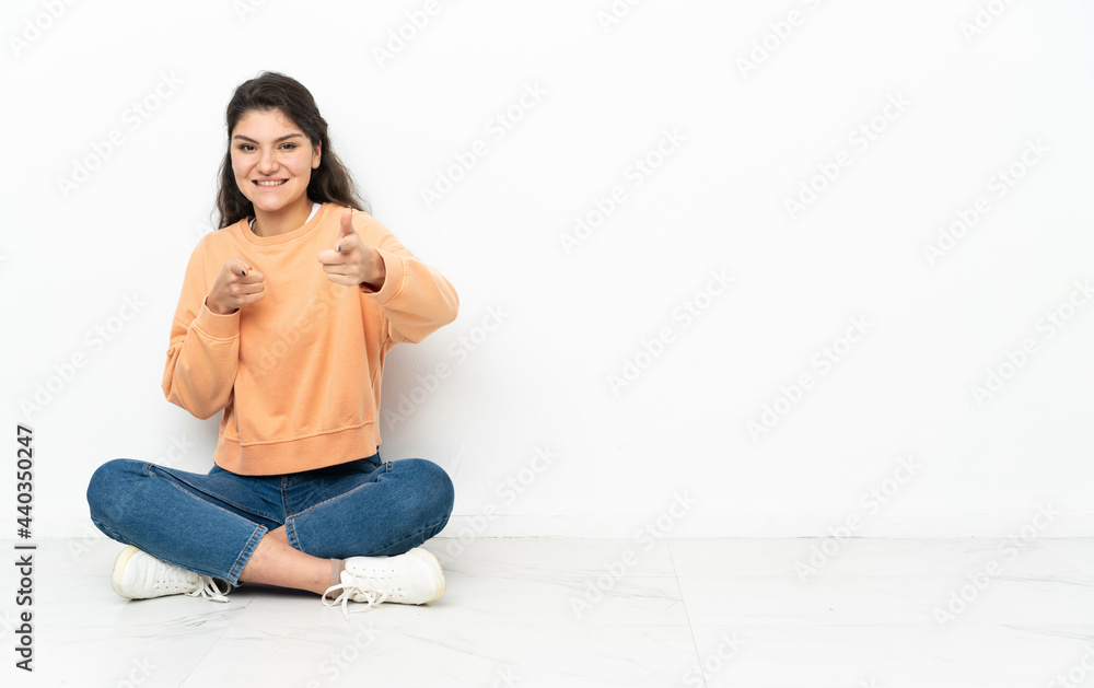 Teenager Russian girl sitting on the floor pointing to the front and smiling Teenager Russian girl sitting on the floor pointing to the front and smiling