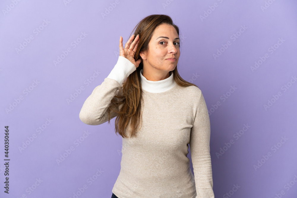 Middle age Brazilian woman isolated on purple background listening to something by putting hand on the ear Middle age Brazilian woman isolated on purple background listening to something by putting hand on the ear