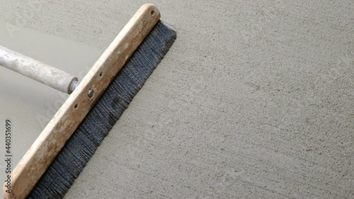 Newly poured cement concrete sidewalk is finished with a slightly rough walking surface, by the use of a wide push broom that is pulled lightly over it. Closeup clip from overhead perspective.