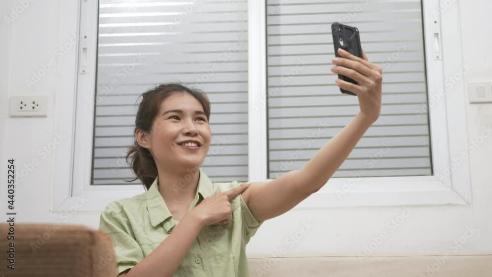 Asian young woman use smartphone video call to friend she pointing to adhesive plaster on arm her vaccinated certificate after getting vaccine prevent at home Asian young woman use smartphone video call to friend she pointing to adhesive plaster on arm her vaccinated certificate after getting vaccine prevent at home