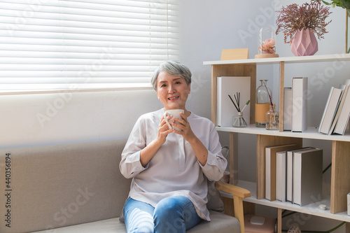 Senior woman sitting on sofa and drinking coffee next to the window.