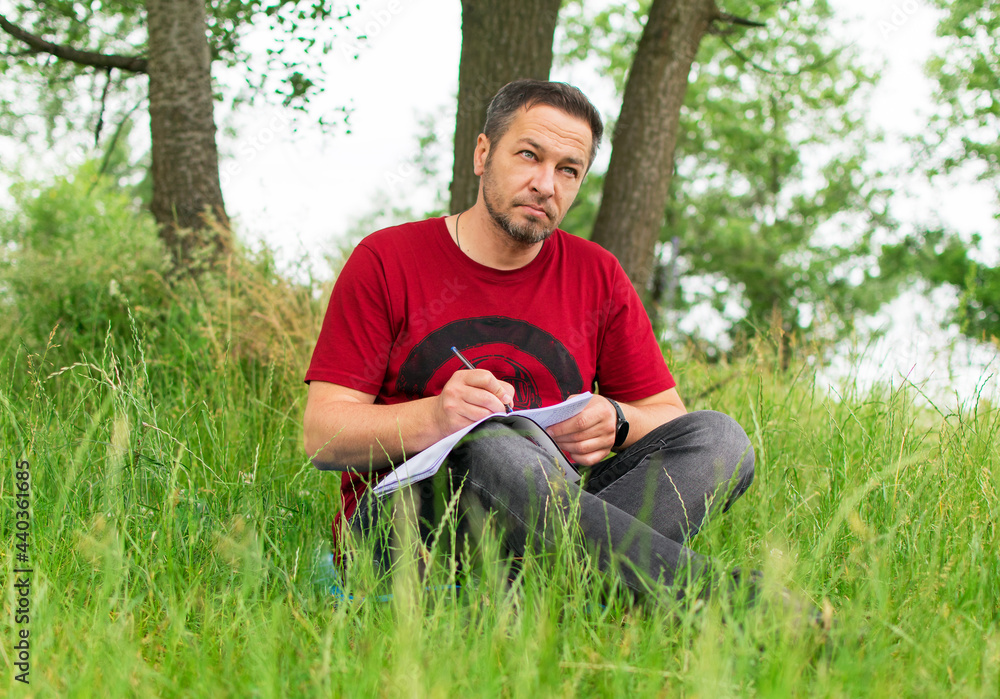 A man in the park, sitting in the grass and writing with a pen in an agenda. A man in the park, sitting in the grass and writing with a pen in an agenda.