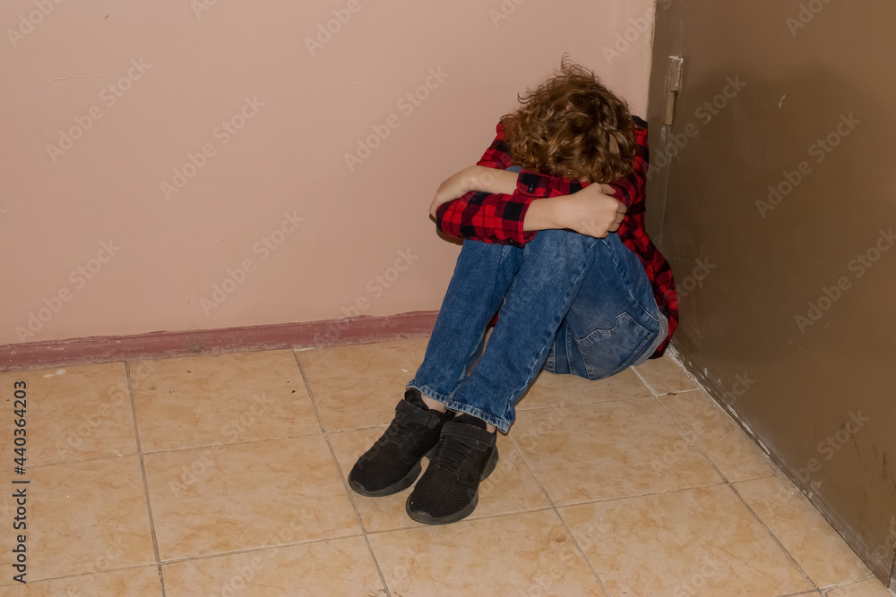 Empty space for the text. A frustrated teenager 11-13 is sitting on the floor near the door in the entrance. Empty space for the text. A frustrated teenager 11-13 is sitting on the floor near the door in the entrance.