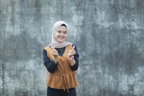 Portrait of Asian muslim woman smiling at camera and making love or heart sign gesture with her hand