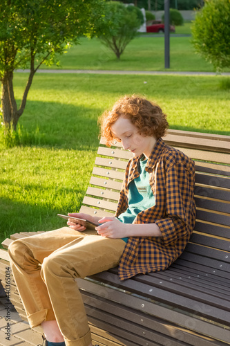Teenager 12-14 with a tablet is sitting on a bench outdoors