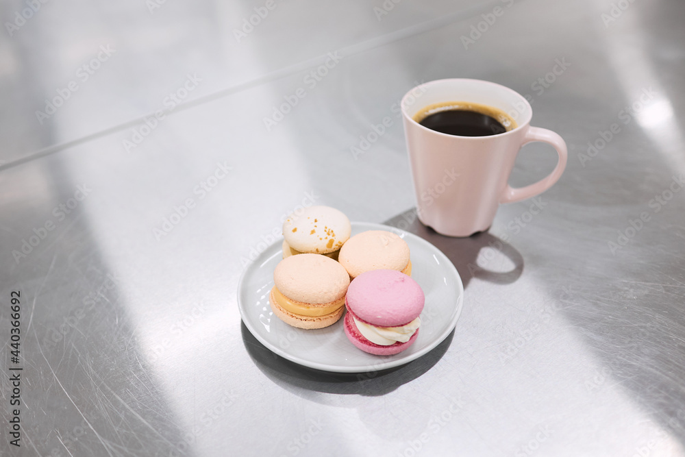 A cup of hot coffee and a saucer of bright macaroons