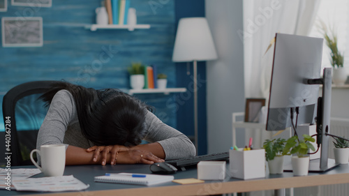 Disappointed workaholic student sleeeping on desk table in living room after working remote from home at job project deadline. Workaholic exhausted young african american woman searching online photo