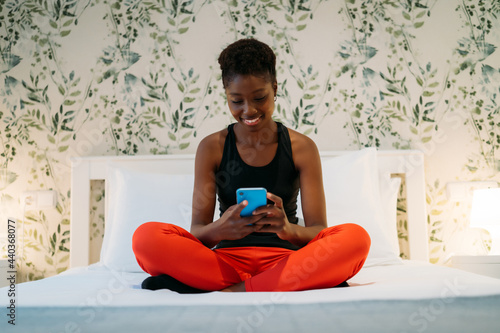 young african american woman smiling using her mobile on bed