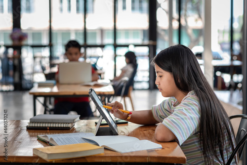 Side view of a girl holding a pen pointing at the tablet screen The book is placed on the table the sides are blurred.