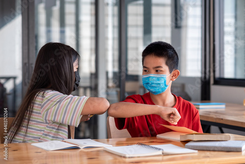 Asian male students and female students study together in the classroom arms touch each other wear a mask to prevent germs.