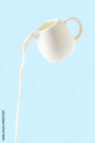 pouring milk from milk jug isolated on blue background