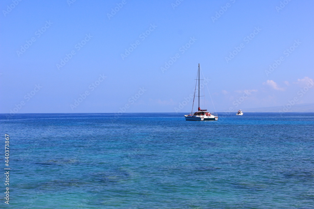 ハワイ島（ビッグアイランド）、青い海、青い空、白い雲。帆を降ろしたヨットが一艘。