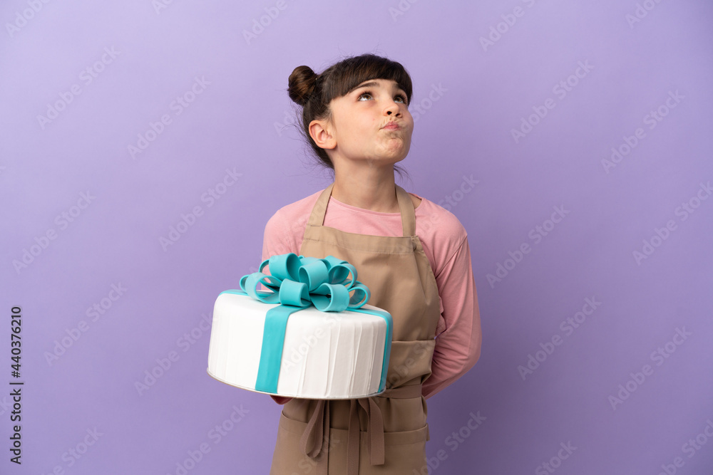 Pastry little girl holding a big cake isolated on purple background and looking up