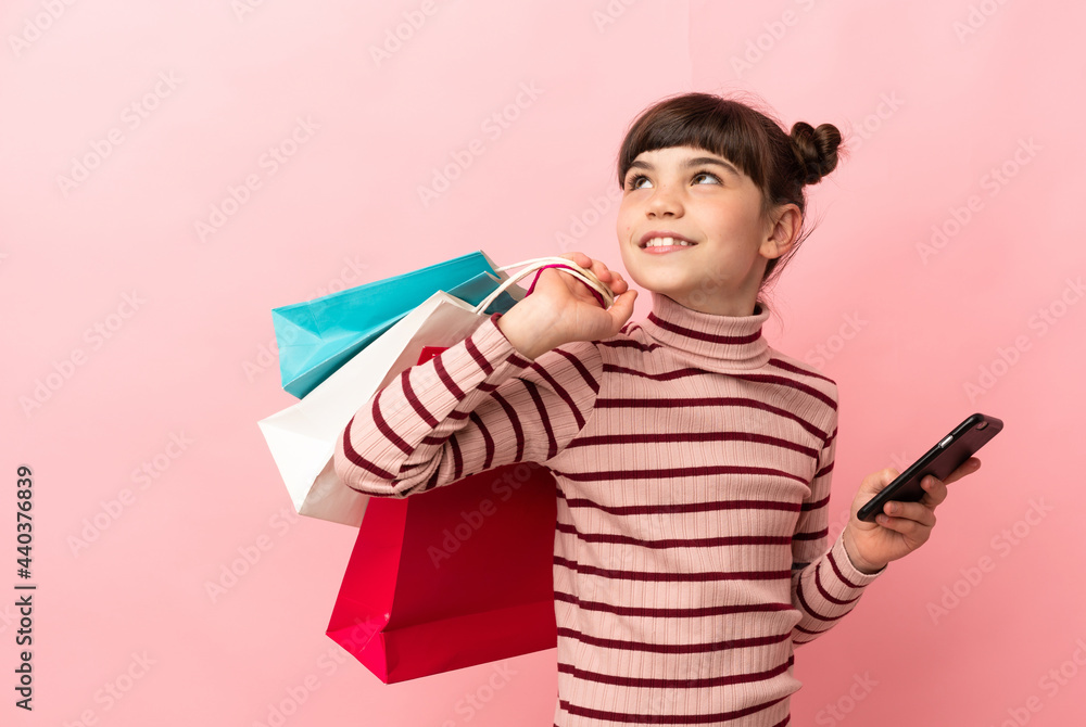 Little caucasian girl isolated on pink background holding shopping bags and a mobile phone Little caucasian girl isolated on pink background holding shopping bags and a mobile phone