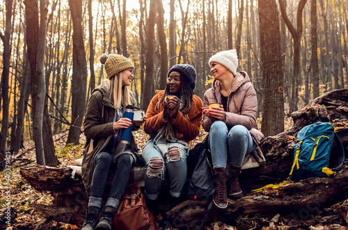 Three female friends resting after hiking in forest sitting on collapsed trunk and drinking tea. © Zoran Zeremski