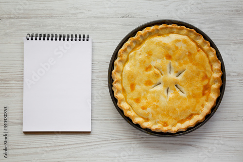 A Piece of Chicken Pot Pie, blank notepad on a white wooden surface, top view. Flat lay, overhead, from above.