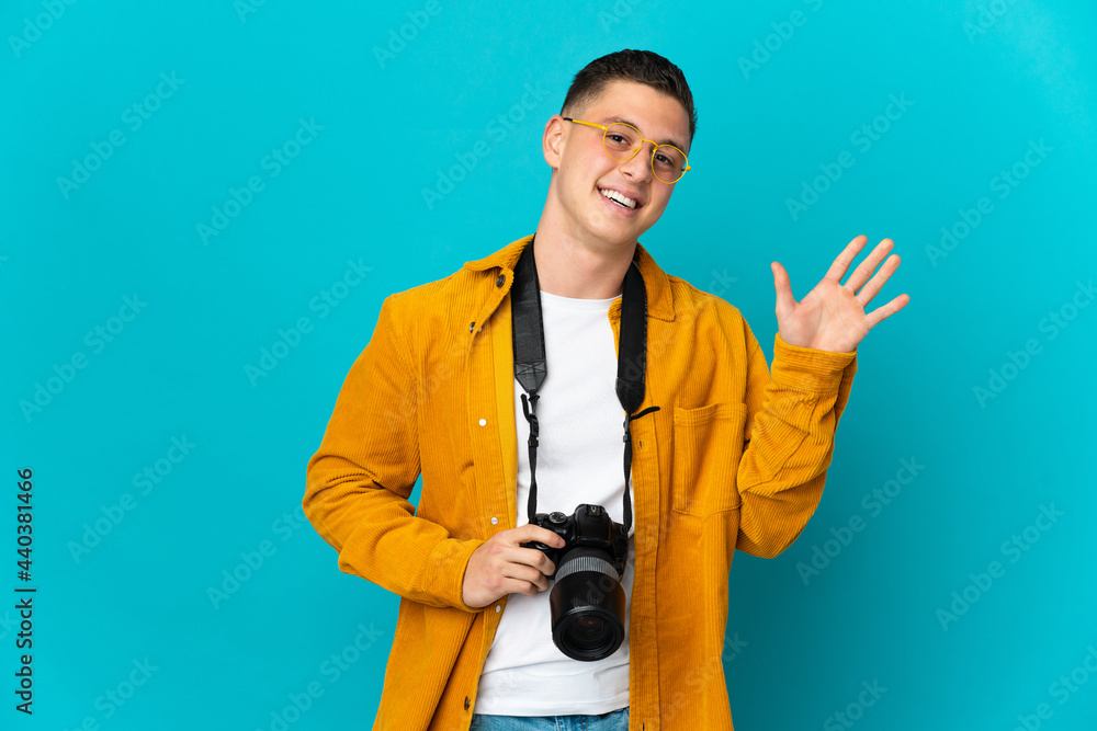 Young caucasian photographer man isolated on blue background saluting with hand with happy expression Young caucasian photographer man isolated on blue background saluting with hand with happy expression