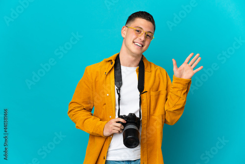 Young caucasian photographer man isolated on blue background saluting with hand with happy expression