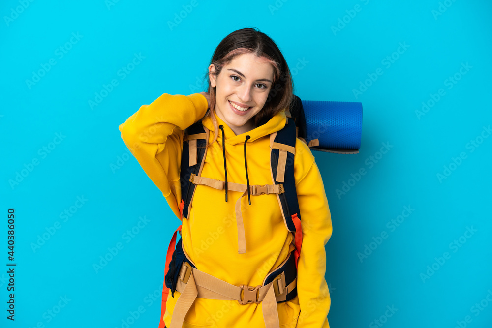 Young mountaineer woman with a big backpack isolated on blue background laughing Young mountaineer woman with a big backpack isolated on blue background laughing