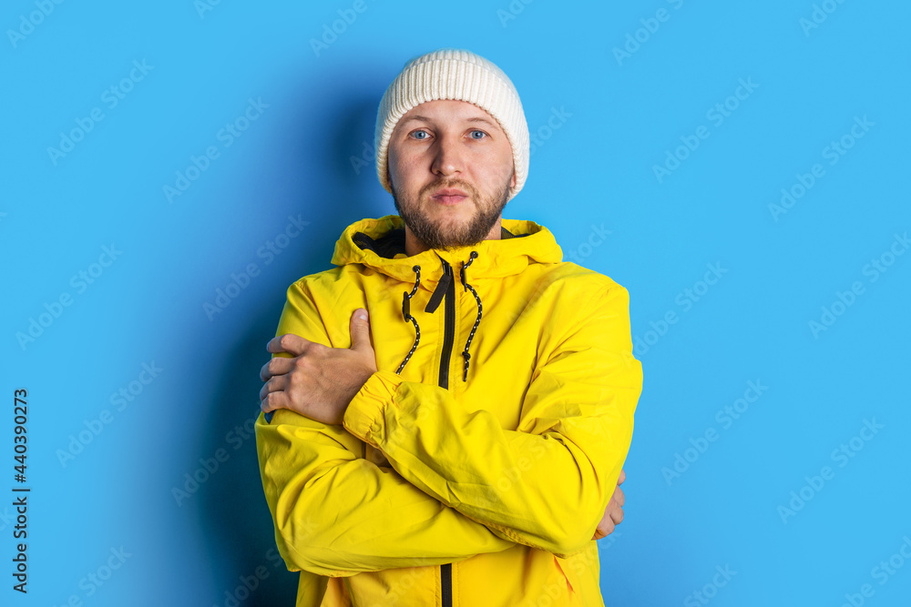 pensive young man in yellow jacket holds his arms crossed on a blue background pensive young man in yellow jacket holds his arms crossed on a blue background