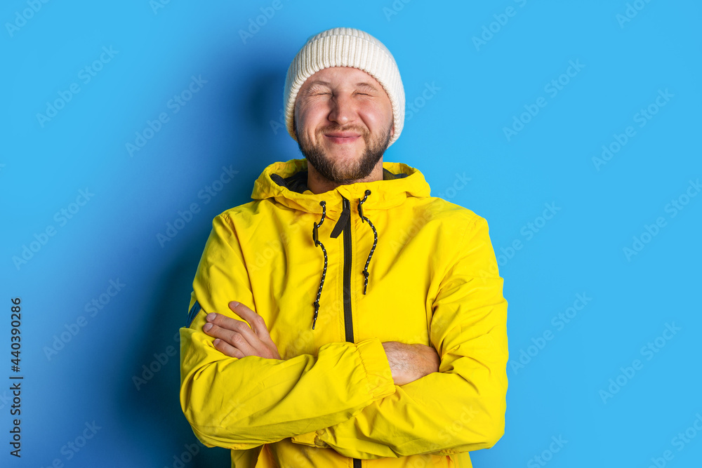 young man in a yellow jacket with closed eyes holds his arms crossed on a blue background young man in a yellow jacket with closed eyes holds his arms crossed on a blue background
