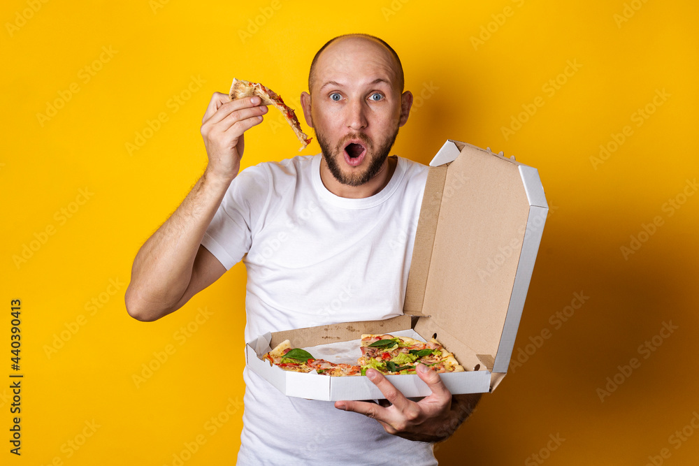 Surprised young man took out a piece of pizza from the packaging on a yellow background Surprised young man took out a piece of pizza from the packaging on a yellow background
