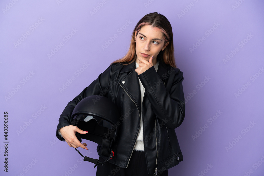 Young caucasian woman holding a motorcycle helmet isolated on purple background and looking up Young caucasian woman holding a motorcycle helmet isolated on purple background and looking up