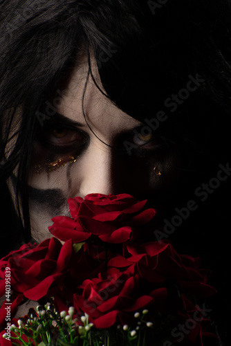 Bride cadaver with black veil holding a bouquet of red roses, black background, Low Key portrait, selective focus.
