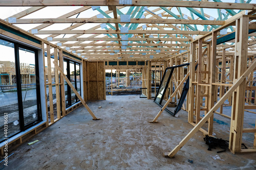 The inside of a house during the early stages of construction, some windows installed, braces holding the frame in place, and another house in the next lot that is also beginning to be built.