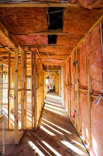 Inside a house under construction, the frame has been erected, plumbing, gas and electrical run. Insulation being installed in the ceiling and walls before plasterboard covers all of the walls.