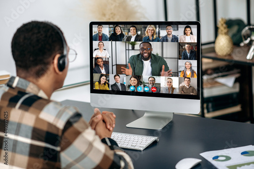 Online video communication. View over a man's shoulder on a computer screen with multiracial people, communicating by video call, a group of partners discuss a project, distant business meeting
