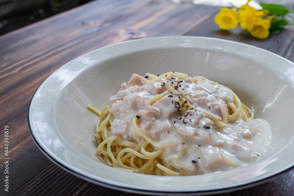 spaghetti carbonara, a delicious mix of ham, bacon and hot cheese, served in a white plate on a ready to eat wooden table. Delicious spaghetti with carbonara sauce mixed with ham, bacon and cheese. spaghetti carbonara, a delicious mix of ham, bacon and hot cheese, served in a white plate on a ready to eat wooden table. Delicious spaghetti with carbonara sauce mixed with ham, bacon and cheese.