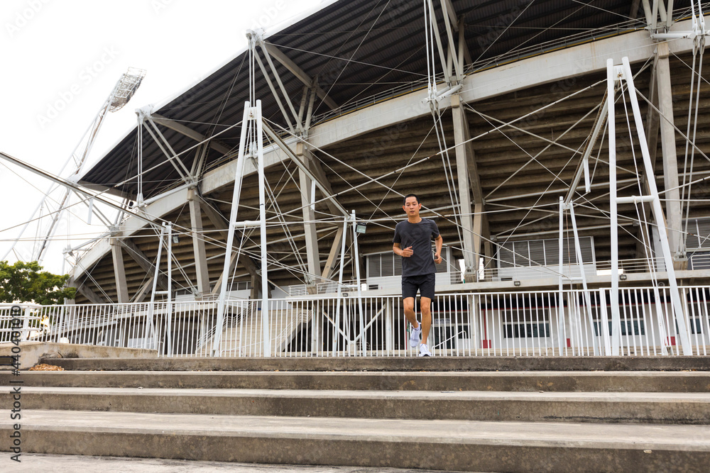 Young athlete asian man running in front of the stadium. The man trains outdoors. Preparing for the marathon.